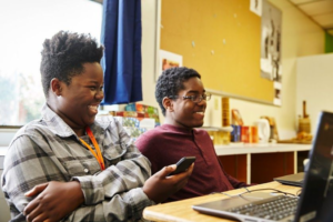Two teens smiling at laptop in classroom