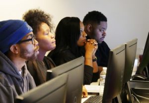 Four adults attentively working at computer monitors