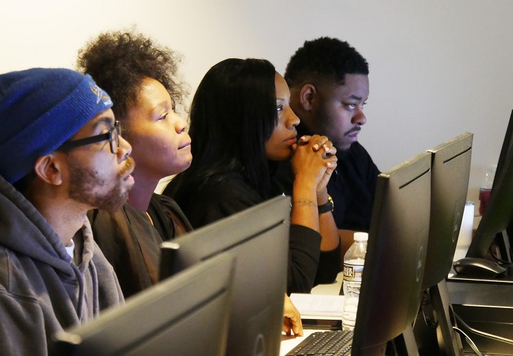 Four adults attentively working at computer monitors